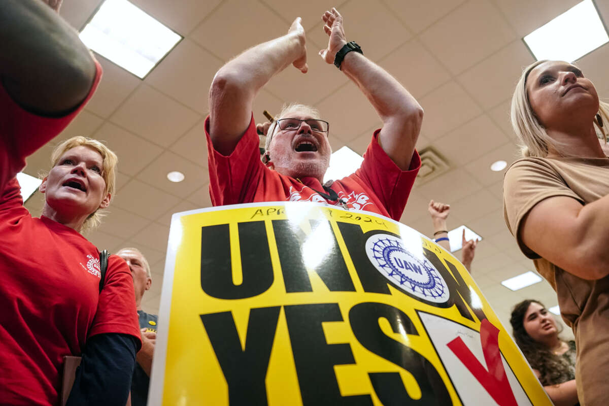 A union member stands to applaud while wearing a sandwich board with text reading "UNION: YES"