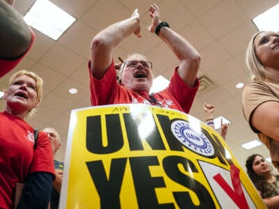 A union member stands to applaud while wearing a sandwich board with text reading "UNION: YES"