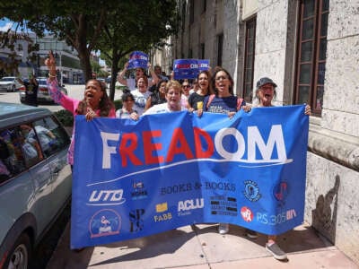 People chant and march behind a banner reading "FREADOM"