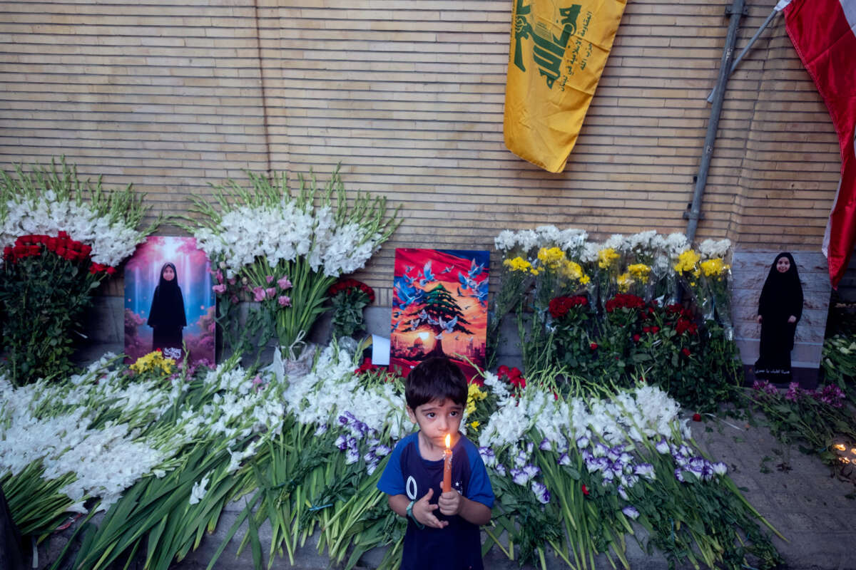 A boy holds a candle while standing in front of a memorial for a slain Lebanese girl