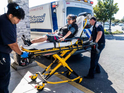 A patient is wheeled toward an ambulance by paramedics