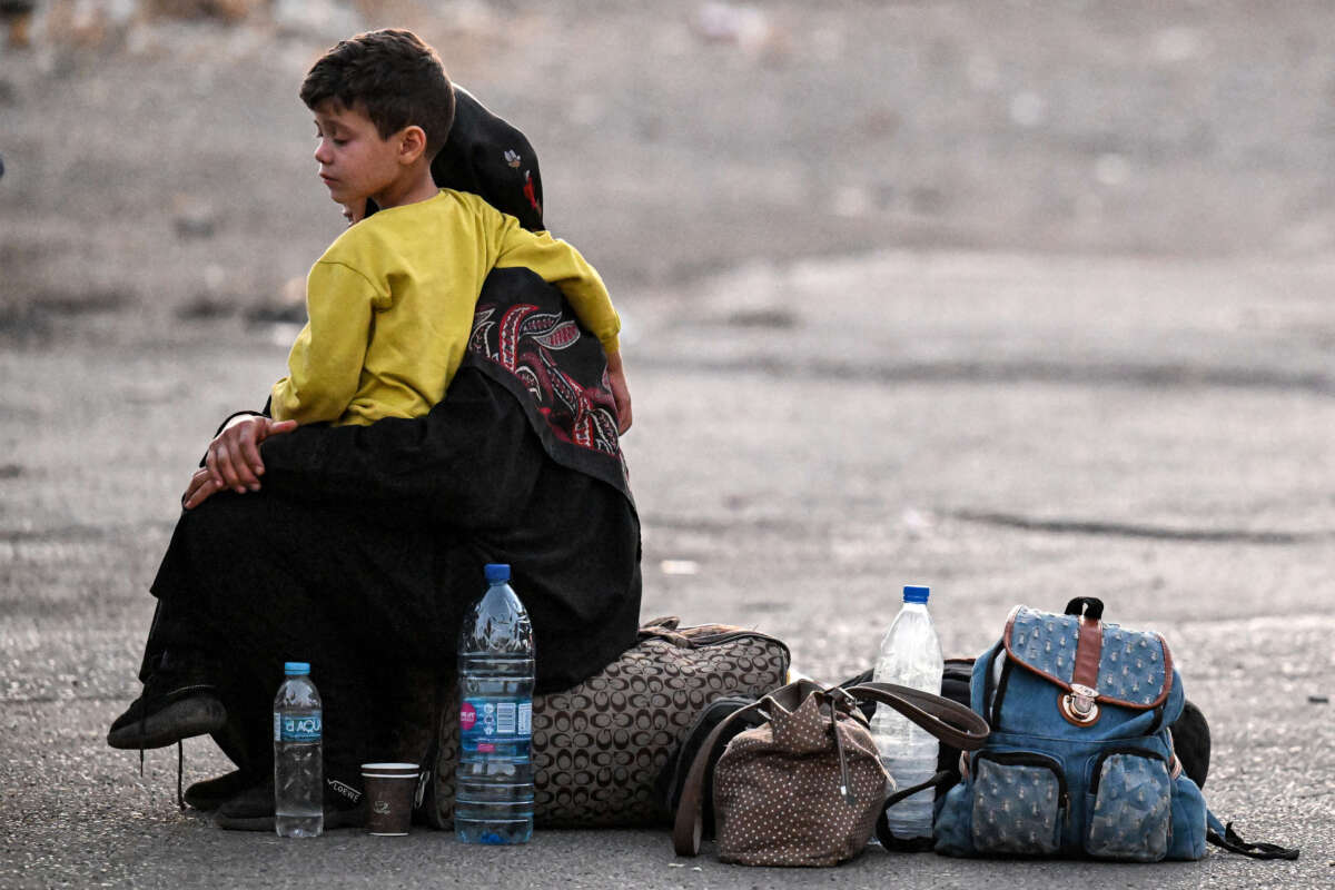 A woman sits with a child on her lap next to bags on the ground as people fleeing from Lebanon arrive on the Syrian side of the border with Lebanon in Jdeidat Yabus in southwestern Syria, on September 24, 2024.