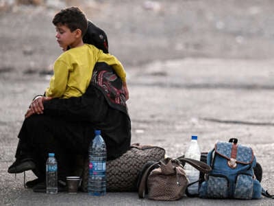 A woman sits with a child on her lap next to bags on the ground as people fleeing from Lebanon arrive on the Syrian side of the border with Lebanon in Jdeidat Yabus in southwestern Syria, on September 24, 2024.