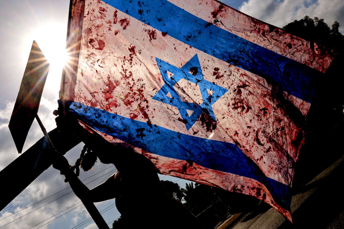 A demonstrator raises an Israeli national flag smeared with red paint as others block traffic on a main road during an anti-government protest in front of the Israeli defense ministry in Tel Aviv, on September 13, 2024.