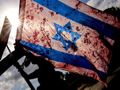 A demonstrator raises an Israeli national flag smeared with red paint as others block traffic on a main road during an anti-government protest in front of the Israeli defense ministry in Tel Aviv, on September 13, 2024.