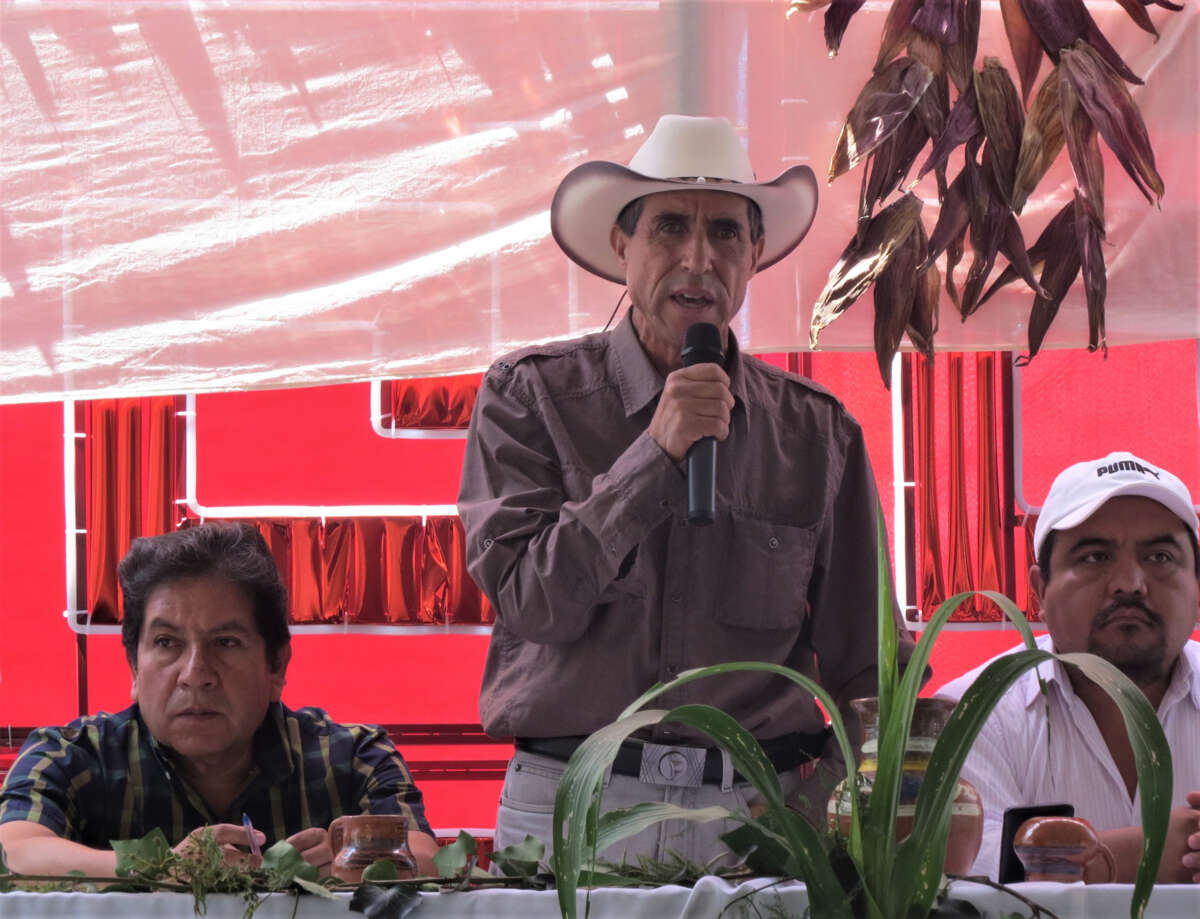 A man in a rancher hat stands and speaks into a microphone