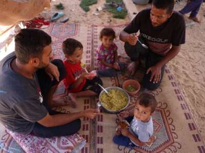 Displaced Palestinians sit for a meal at a makeshift camp for the displaced in Khan Yunis in the southern Gaza Strip on September 11, 2024.