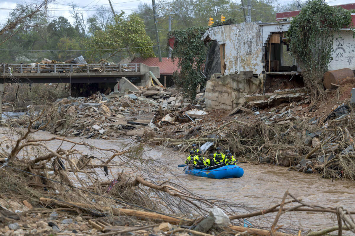 An inflatable raft carrying people floats through floodwaters beside a partially-destroyed building