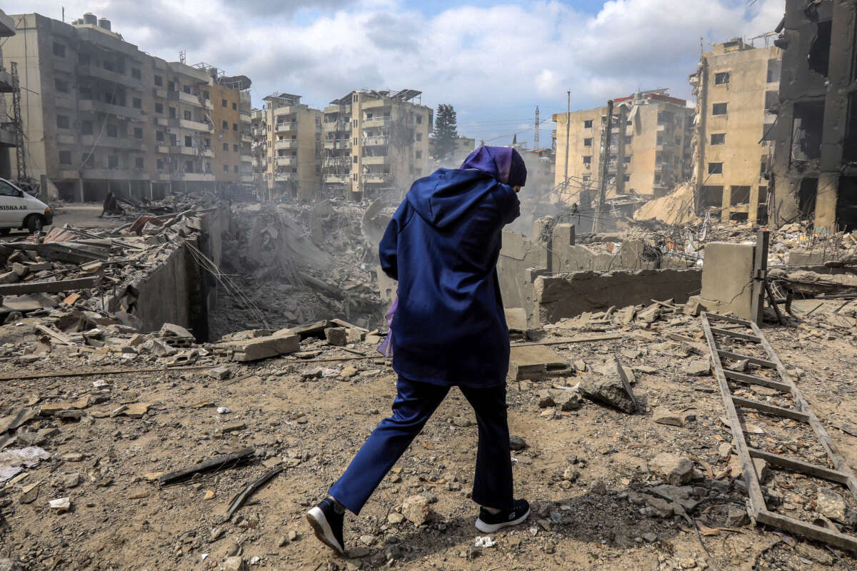 A woman walks past a crater where a collapsed building stood following an overnight Israeli air strike on the neighbourhood of Kafaat in Beirut's southern suburbs, on October 7, 2024.