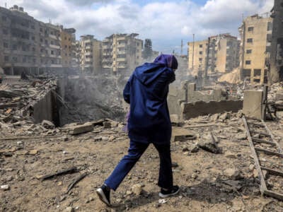 A woman walks past a crater where a collapsed building stood following an overnight Israeli air strike on the neighbourhood of Kafaat in Beirut's southern suburbs, on October 7, 2024.