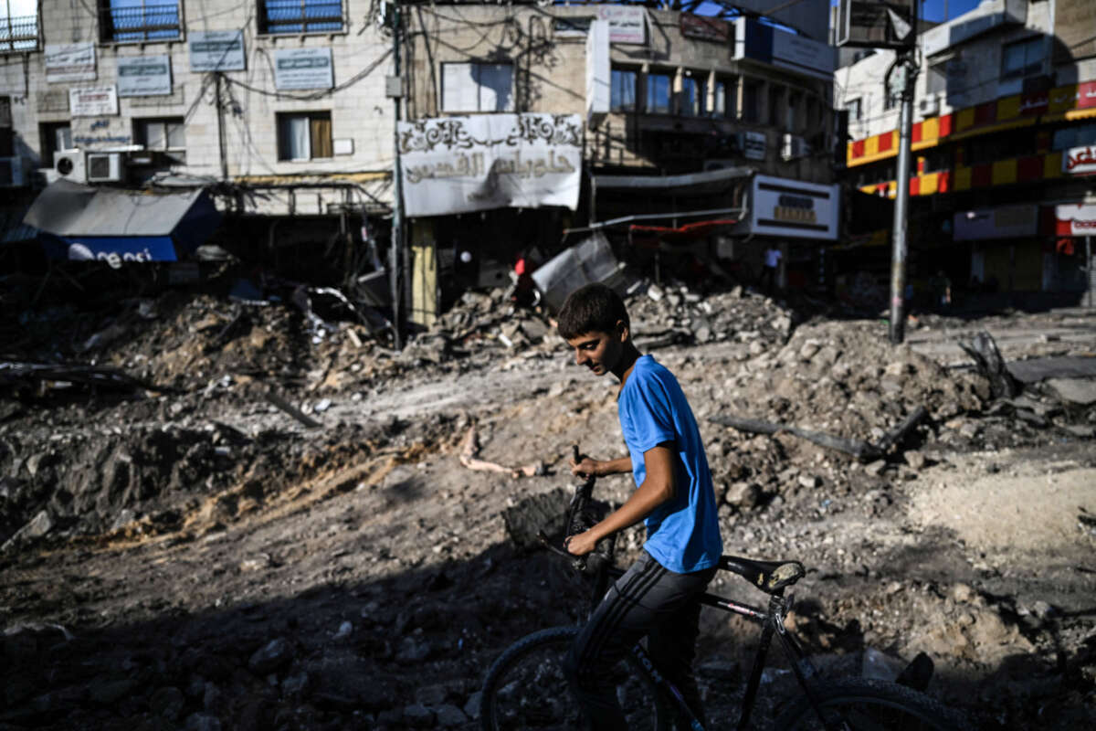 A Palestinian child pushes his bike next to a street and past shops damaged by bulldozers during an Israeli raid in the center of Jenin in the occupied West Bank on September 2, 2024.