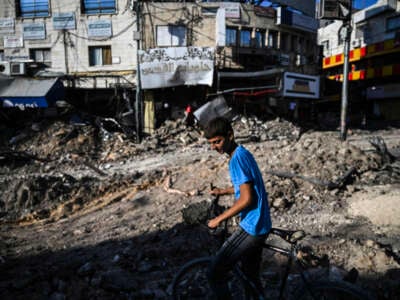 A Palestinian child pushes his bike next to a street and past shops damaged by bulldozers during an Israeli raid in the center of Jenin in the occupied West Bank on September 2, 2024.