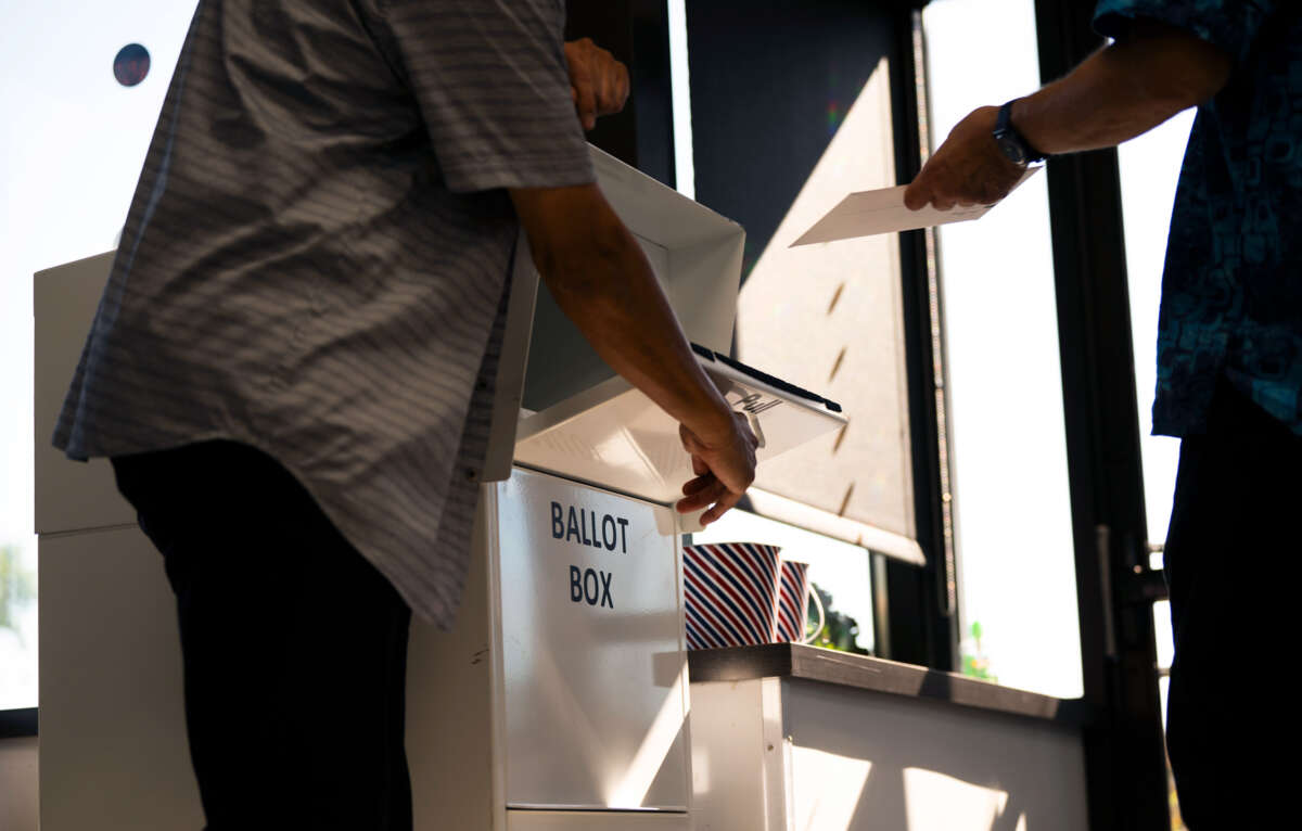 A person holds open a ballot box while another inserts their ballot