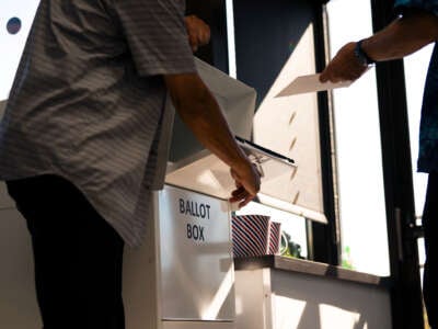 A person holds open a ballot box while another inserts their ballot