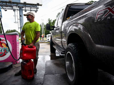 A man fills jugs with gas while standing next to his truck