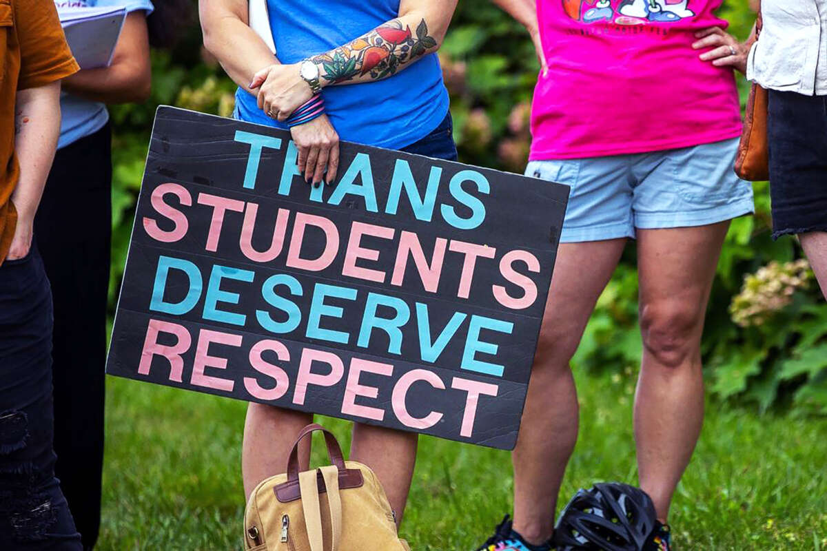 A person holds a sign reading "TRANS STUDENTS DESERVE RESPECT" during an outdoor demonstration