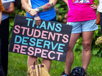 A person holds a sign reading "TRANS STUDENTS DESERVE RESPECT" during an outdoor demonstration