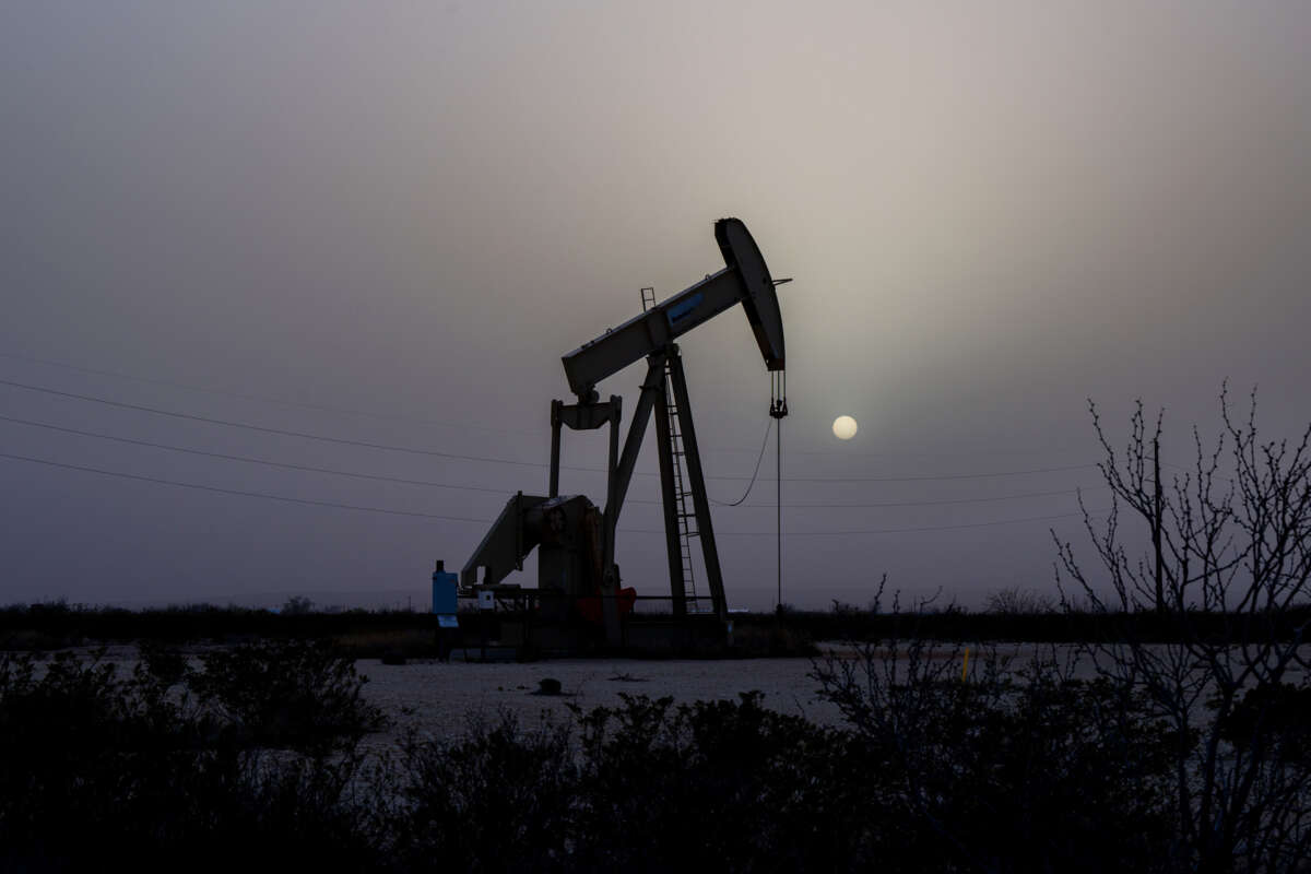 A pumpjack is seen against a grey sky and a hazy sun