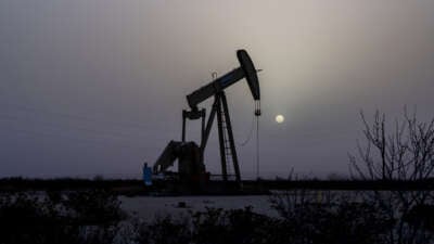 A pumpjack is seen against a grey sky and a hazy sun