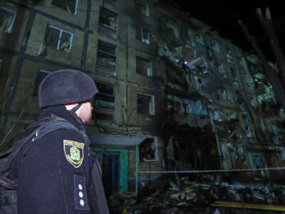 A cop looks at a building with a partially-destroyed wall