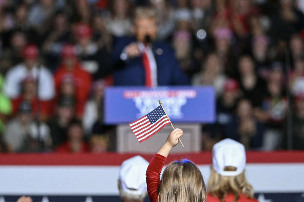 A child holds a small American flag as Republican presidential candidate and former President Donald Trump speaks during a campaign rally at the Ryder Center for Health and Physical Education at Saginaw Valley State University in Saginaw, Michigan, on October 3, 2024.