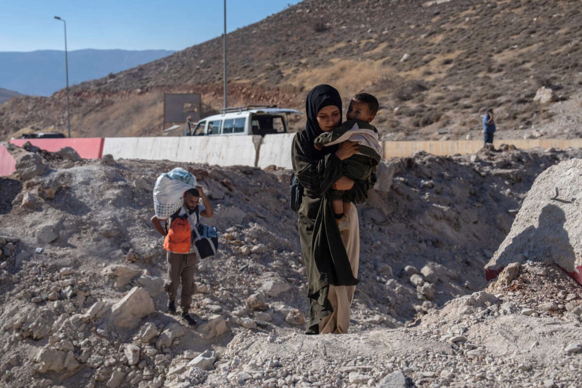 A woman carries a child through the crater from an Israeli air strike as she makes her way across the border from Lebanon into Syria on October 5, 2024, in Masnaa, Lebanon.