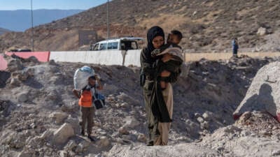 A woman carries a child through the crater from an Israeli air strike as she makes her way across the border from Lebanon into Syria on October 5, 2024, in Masnaa, Lebanon.