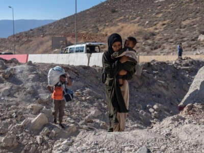 A woman carries a child through the crater from an Israeli air strike as she makes her way across the border from Lebanon into Syria on October 5, 2024, in Masnaa, Lebanon.