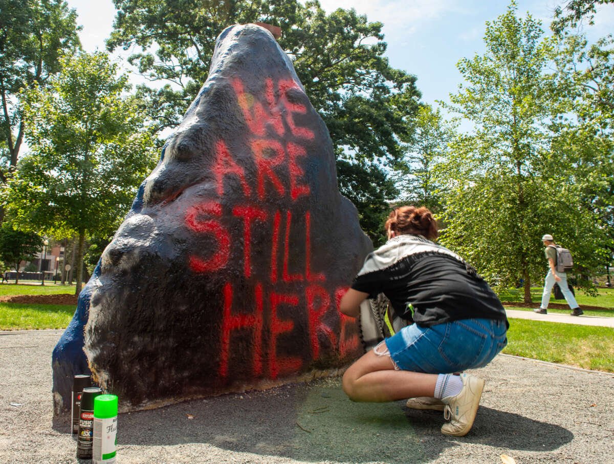 A UConn student spray paints "We Are Still Here" on UConn's Spirit Rock during a pro-Palestine rally on campus as classes begin on August 26, 2024.