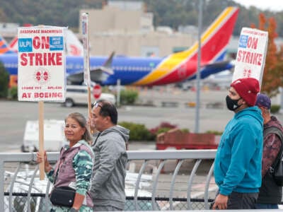 People carry Boeing strike signs as they walk past parked Boeing 737 planes near Boeing Field following a strike rally for the International Association of Machinists and Aerospace Workers at the Seattle Union Hall in Seattle, Washington, on October 15, 2024.