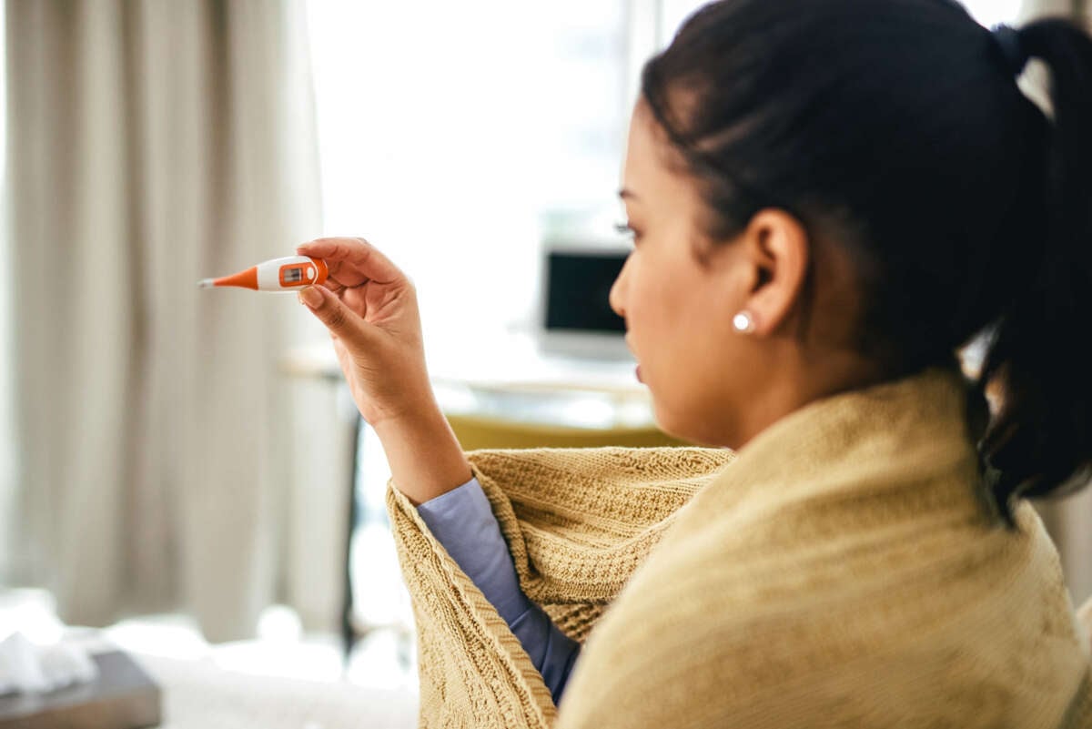 Woman wrapped in blanket checks a thermometer to see if she's sick