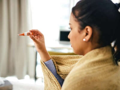 Woman wrapped in blanket checks a thermometer to see if she's sick