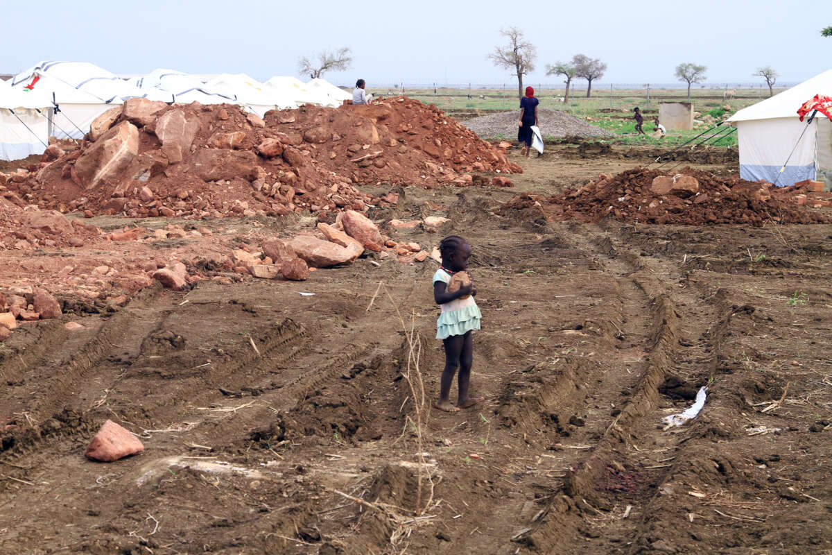 A little girls holds a rock as she stands among rubble