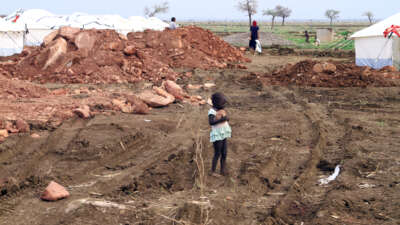 A little girls holds a rock as she stands among rubble