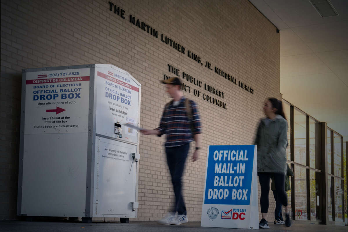 A voter places their vote into a drop box as another voter follows behind them