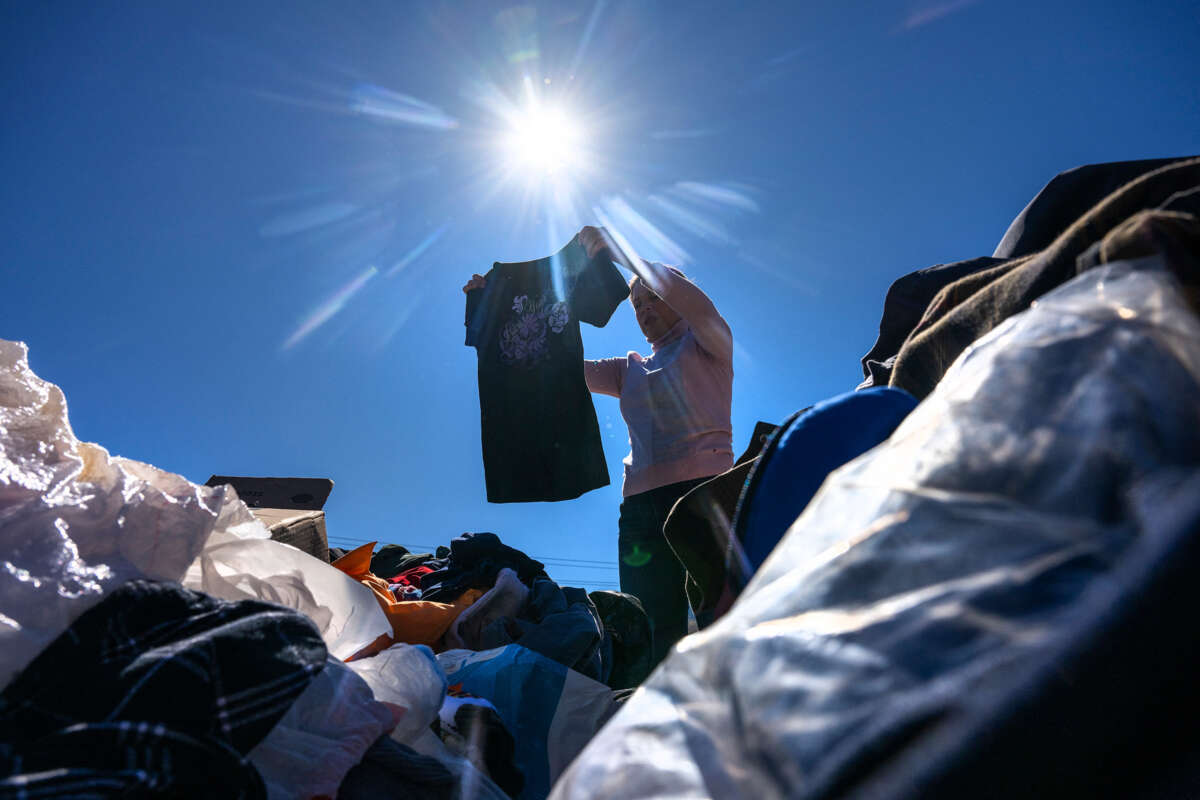 A woman holds up a shirt while standing among a pile of clothing