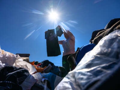 A woman holds up a shirt while standing among a pile of clothing