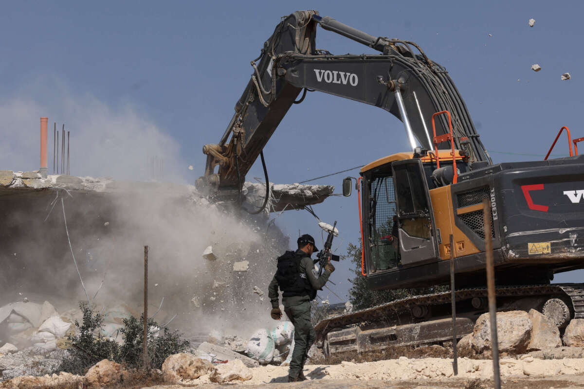 A member of the Israeli security forces walks past a bulldozer demolishing a house belonging to Palestinians, located in the area C, which lies under Israel's military control since 1967, in Yatta village in the southern area of the occupied West Bank, on November 6, 2024.