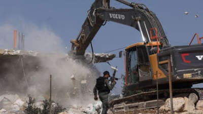 A member of the Israeli security forces walks past a bulldozer demolishing a house belonging to Palestinians, located in the area C, which lies under Israel's military control since 1967, in Yatta village in the southern area of the occupied West Bank, on November 6, 2024.