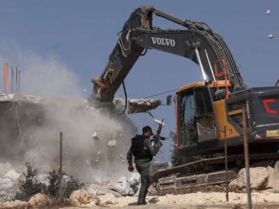 A member of the Israeli security forces walks past a bulldozer demolishing a house belonging to Palestinians, located in the area C, which lies under Israel's military control since 1967, in Yatta village in the southern area of the occupied West Bank, on November 6, 2024.