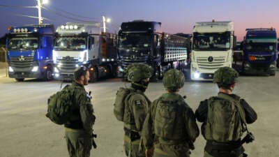 Israeli soldiers stand guard as trucks loaded with humanitarian aid delivered from Jordan wait to cross into Gaza on the border between Israel and the northern Gaza Strip, through the Israeli-controlled Erez crossing on October 21, 2024. (Photo taken during a controlled tour by the Israeli military.)