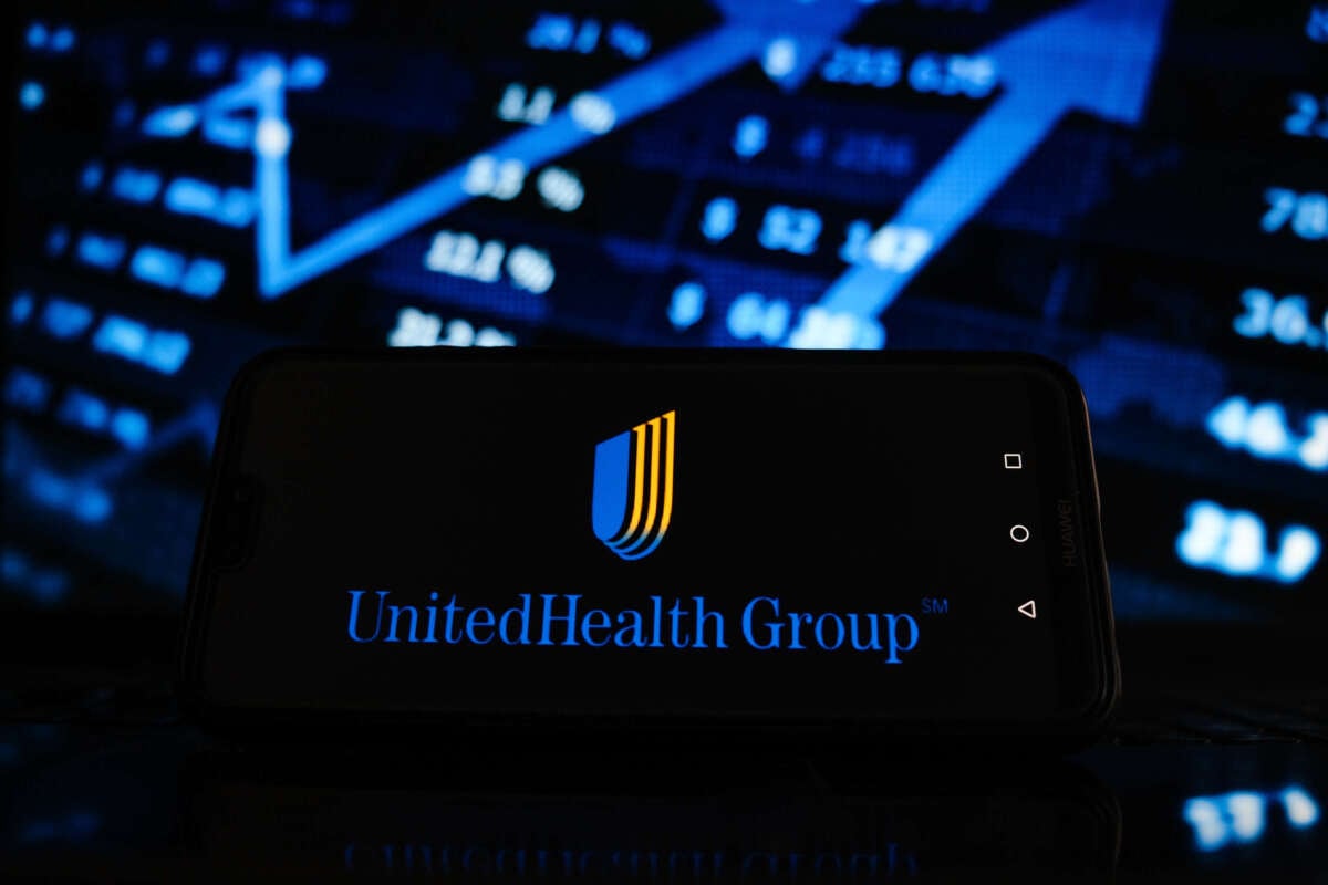 In this photo illustration, the United Health Group logo is displayed on a smartphone screen with stock market graphic on the background.