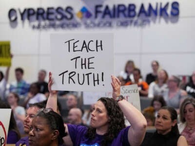 A parent holds a sign reading "TEACH THE TRUTH" during a board of trustees meeting