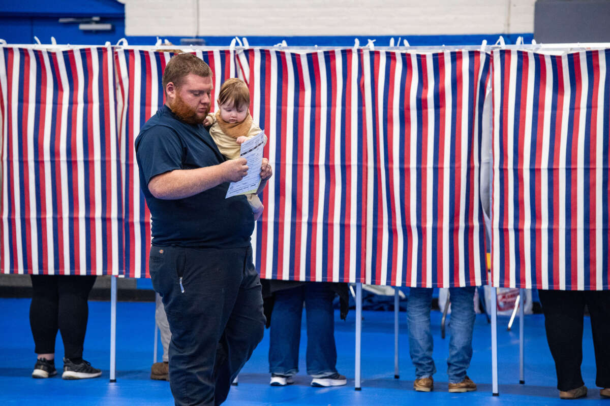 A man and his baby both look at his ballot as he walks through a red, white and blue-spangled polling place