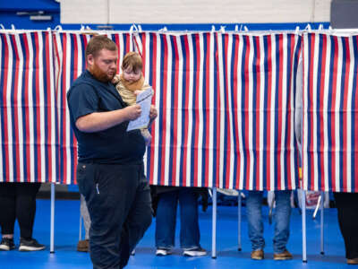 A man and his baby both look at his ballot as he walks through a red, white and blue-spangled polling place