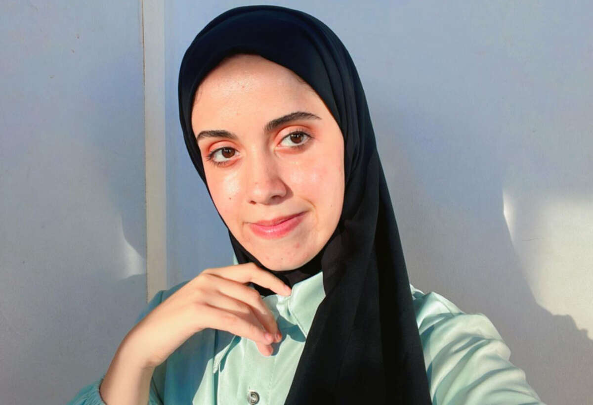 A portrait of a woman wearing a black hijab and a green blouse