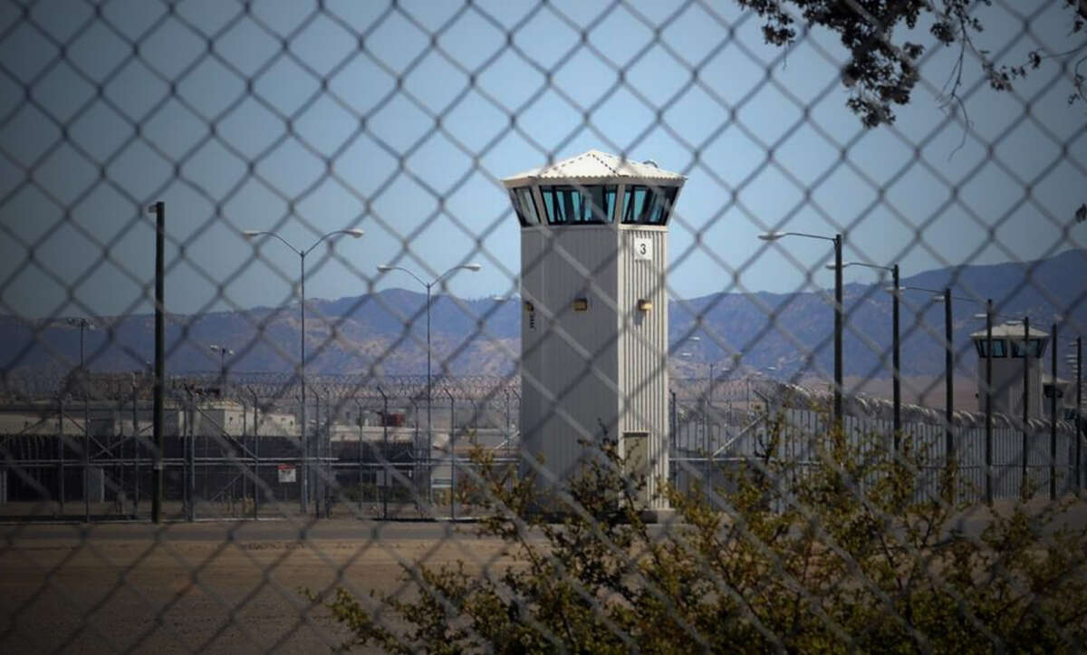 The watchtower of a prison is seen from outside of a chain link fence