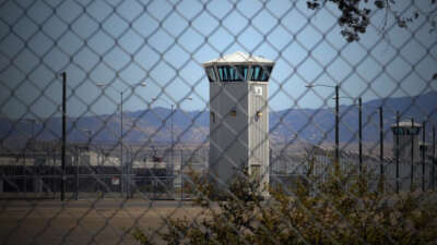 The watchtower of a prison is seen from outside of a chain link fence