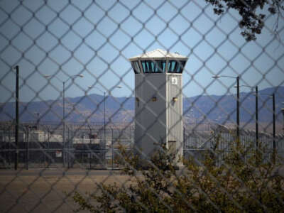 The watchtower of a prison is seen from outside of a chain link fence