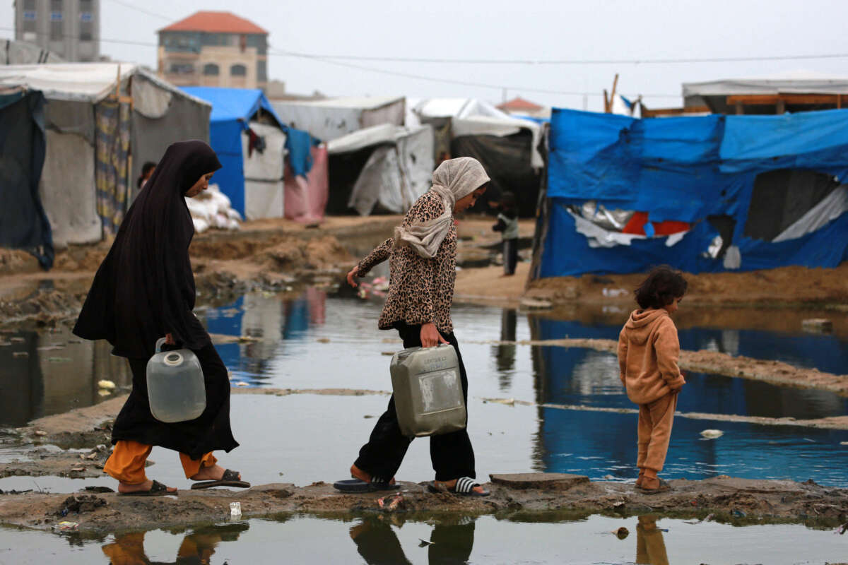 Displaced Palestinians use a dry path to carry water to their tent, following heavy rainfall north of Deir el-Balah in the central Gaza Strip on November 24, 2024.